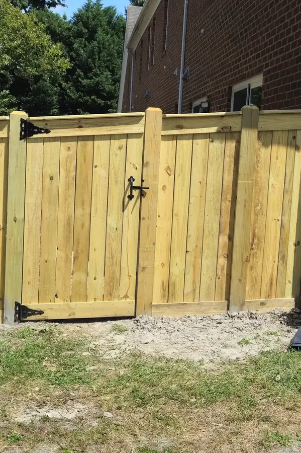 Pressure-treated wood privacy gate with top cap, black strap hinges and a black gravity latch, set in a matching six-foot privacy fence beside a brick house, Hampton Roads, Virginia